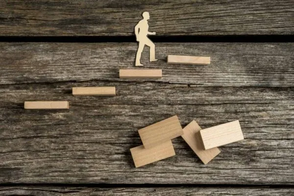 Silhouette cutouts of a man walking up wooden steps with dominos over old rough wooden table surface. | TranSystems Promotes Shawn Turner to Principal and Senior Vice President