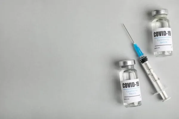 Vials with coronavirus vaccine and syringe on light background, flat lay. Space for text | By the Data: How Covid-19 has Impacted the AEC Industry