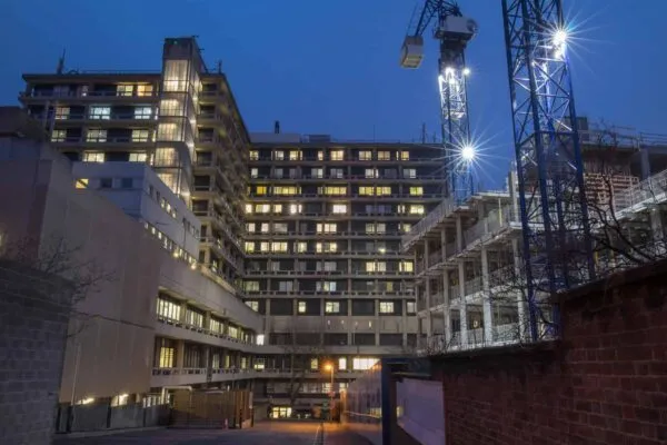 The back side of a central hospital in London with the lights on at dusk. Construction site on the right for residential homes. | Smith Currie Named Construction Law Firm of the Year