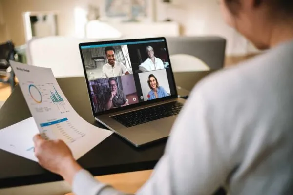 Woman holding a business report working at home having a video conference with colleagues. Over the shoulder view of a businesswoman having online business meeting from home. | Adaptiv Networks Launches SD-WAN Solution for Remote and Mobile Workers