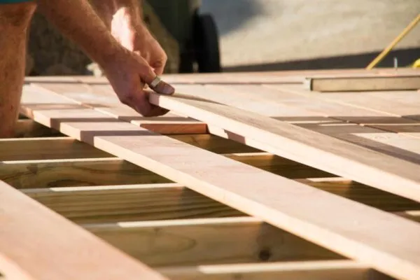 Man placing a plank of wood in a deck home renovation on a warm sunny day | Simpson Strong-Tie has New Tech Bulletin and Webinar to Detail Solutions for Meeting the DCA 6 Residential Wood Deck Construction Guide