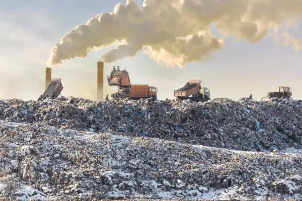 Dump trucks unloading garbage over vast landfill. Smoking industrial stacks on background. Environmental pollution. Outdated method of waste disposal. Survival of times past. | Clean Energy Technologies Becomes EPA Industry Partner As Part of President Biden’s Methane Limitation Program