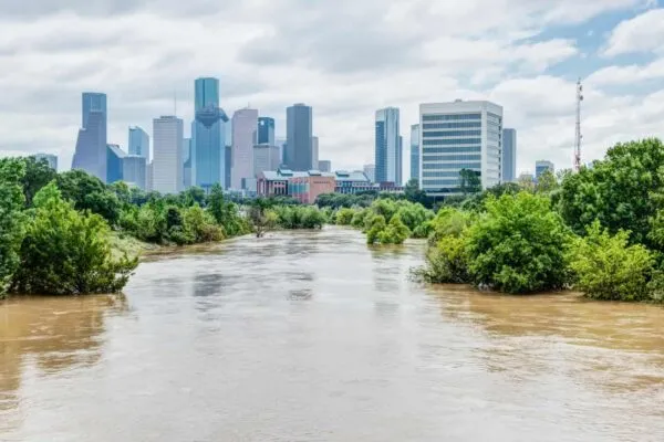 High and fast water rising in Bayou River with downtown Houston in background under cloud blue sky. Heavy rains from Harvey Tropical Hurricane storm caused many flooded areas in greater Houston area. | Rebuilding an Underfunded Community in Houston