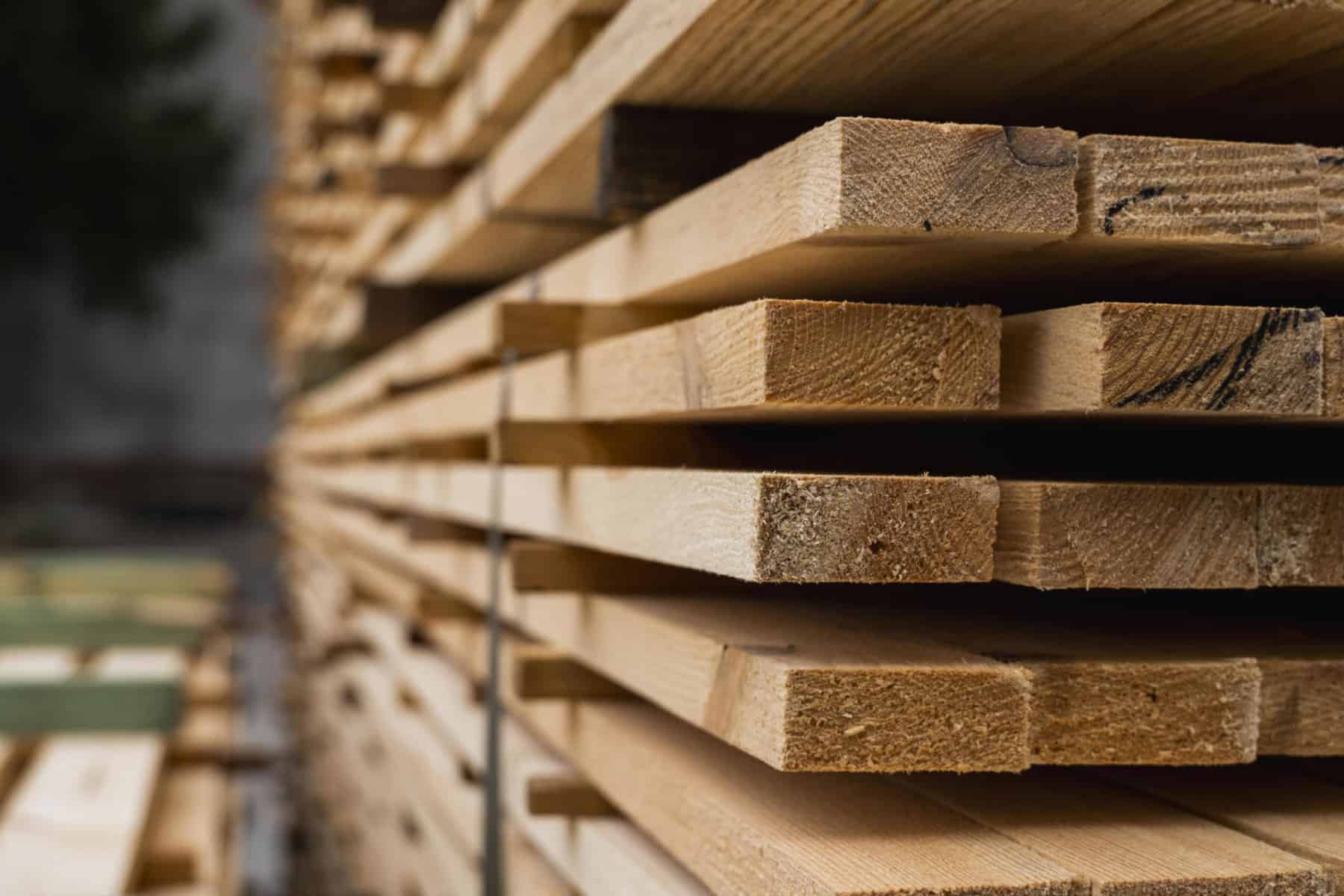 Piles of wooden boards in the sawmill, planking. Warehouse for sawing boards on a sawmill outdoors. Wood timber stack of wooden blanks construction material. Industry | North American launch of AI-powered design software DAISY AI to produce structural timber designs automatically and reduce construction waste by up to 80%.