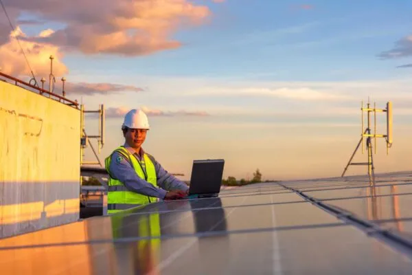 Engineer using laptop at solar panels on rooftop at sunset sky, An engineer working at a photovoltaic farm. Eco technology for electric power | CEMEX INVESTS IN PIONEER SOLAR TECHNOLOGY