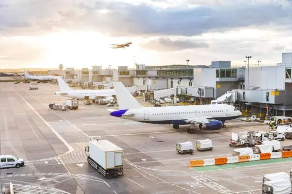 Busy airport view with airplanes and service vehicles at sunset. London airport with aircrafts at gates and taking off, trucks all around and sun setting on background. Travel and industry concepts | Hartsfield-Jackson Publicizes Five Real Estate Properties for Bid