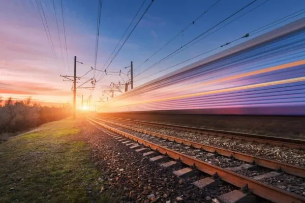 High speed passenger train in motion on railroad at sunset. Blurred commuter train. Railway station against sunny sky. Railroad travel, railway tourism. Rural industrial landscape. Concept | American Track Acquires the Railroad Associates Corp (TRAC)