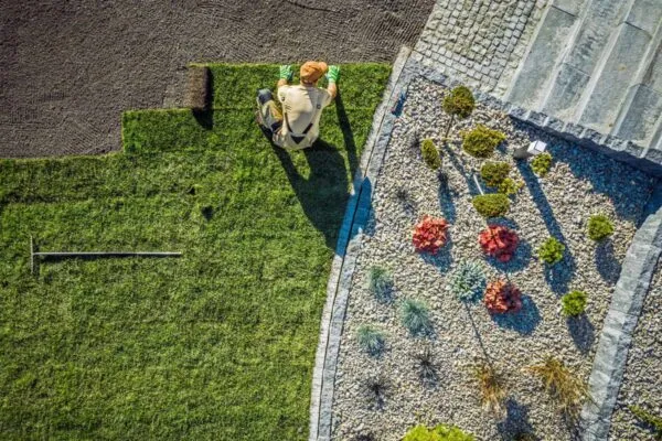 Aerial View Of Male Gardener Laying Rolls Of Sod In Large Area Of Residential Backyard. | LandOpt Shares Strategies to Help Landscape Contractors Save on Fuel Costs