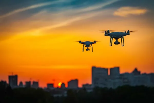 Two drone quad copters with high resolution digital camera flying aerial over spectacular sunset orange sky. Cityscape silhouette with sun goes down in the background.Vehicle at sundown and copy space | The Desire for New Heights