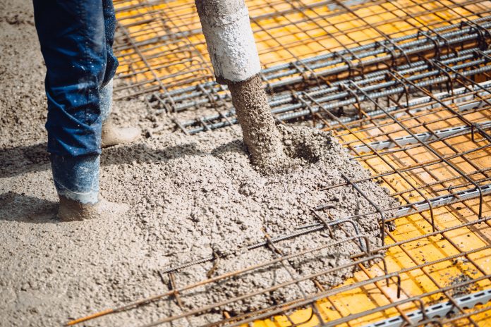 man on construction site, worker pouring concrete with pump tube