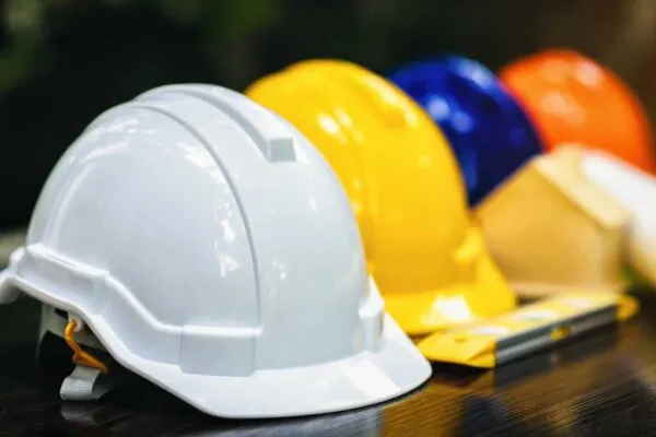 White and colored helmets that have different duties for the safety program of workers in the position of engineers or workers on the table. | Construction Safety Programs and the Labor Shortage
