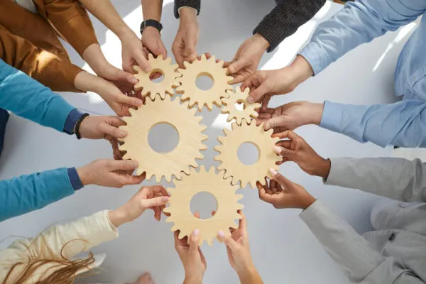Business people or office workers hold wooden gears that symbolize well-coordinated teamwork. Top view close up of hands of multiracial men and women standing in circle. Concept business cooperation | Stantec recognized in the Top 10 globally for climate action by Corporate Knights