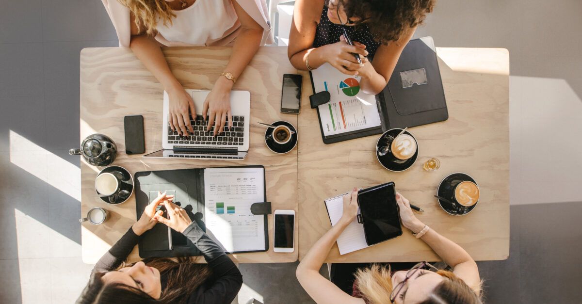 Top view of four women sitting around table in cafe with laptop, digital tablet and documents. Group of women working together in coffee shop. | Leading from the Front: WSP’s Women Leaders are Paving the Way to a More Equitable Future